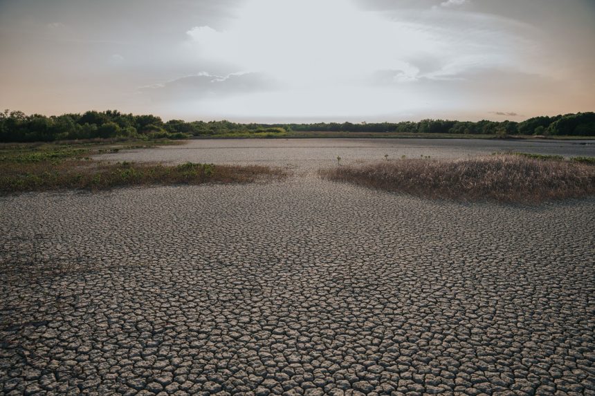Vista aérea de uma paisagem seca e rachada sob céu claro, evidenciando condições de estiagem.