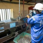 Trabalhador de fábrica opera uma mesa vibratória para separar e processar minério.