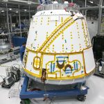 Profissional em uniforme realiza manutenção em uma espaçonave dentro de uma instalação industrial.