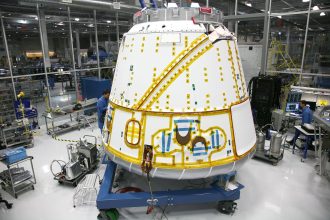 Profissional em uniforme realiza manutenção em uma espaçonave dentro de uma instalação industrial.
