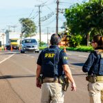 Agentes da Polícia Rodoviária Federal monitoram o trânsito em uma via durante o dia.