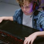 Criança usando teclado, mouse e fones de ouvido enquanto joga no computador.