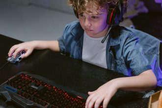 Criança usando teclado, mouse e fones de ouvido enquanto joga no computador.